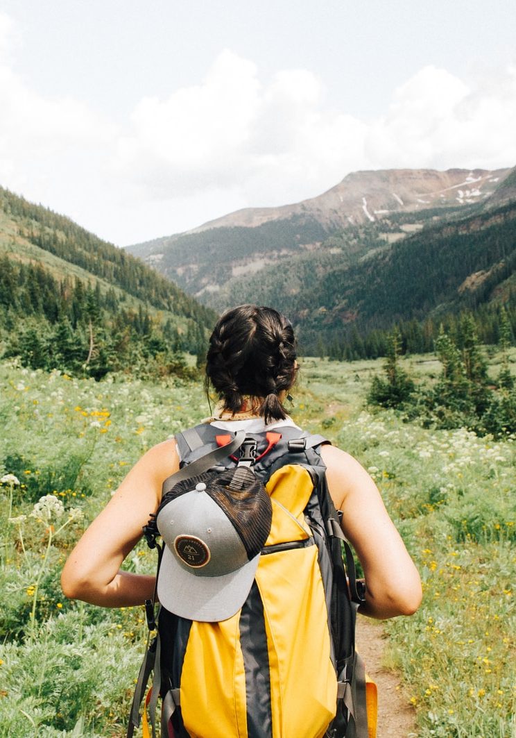 person carrying yellow and black backpack walking between green plants